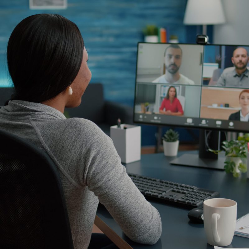 Black student discussing marketing academic ideas with college team having virtual teleconference meeting sitting at desk in living room. Woman working at deadline project during online webinar